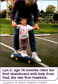 Lyn-Z, age 18 months rides her first skateboard with help from Dad, the late Ron Hawkins.